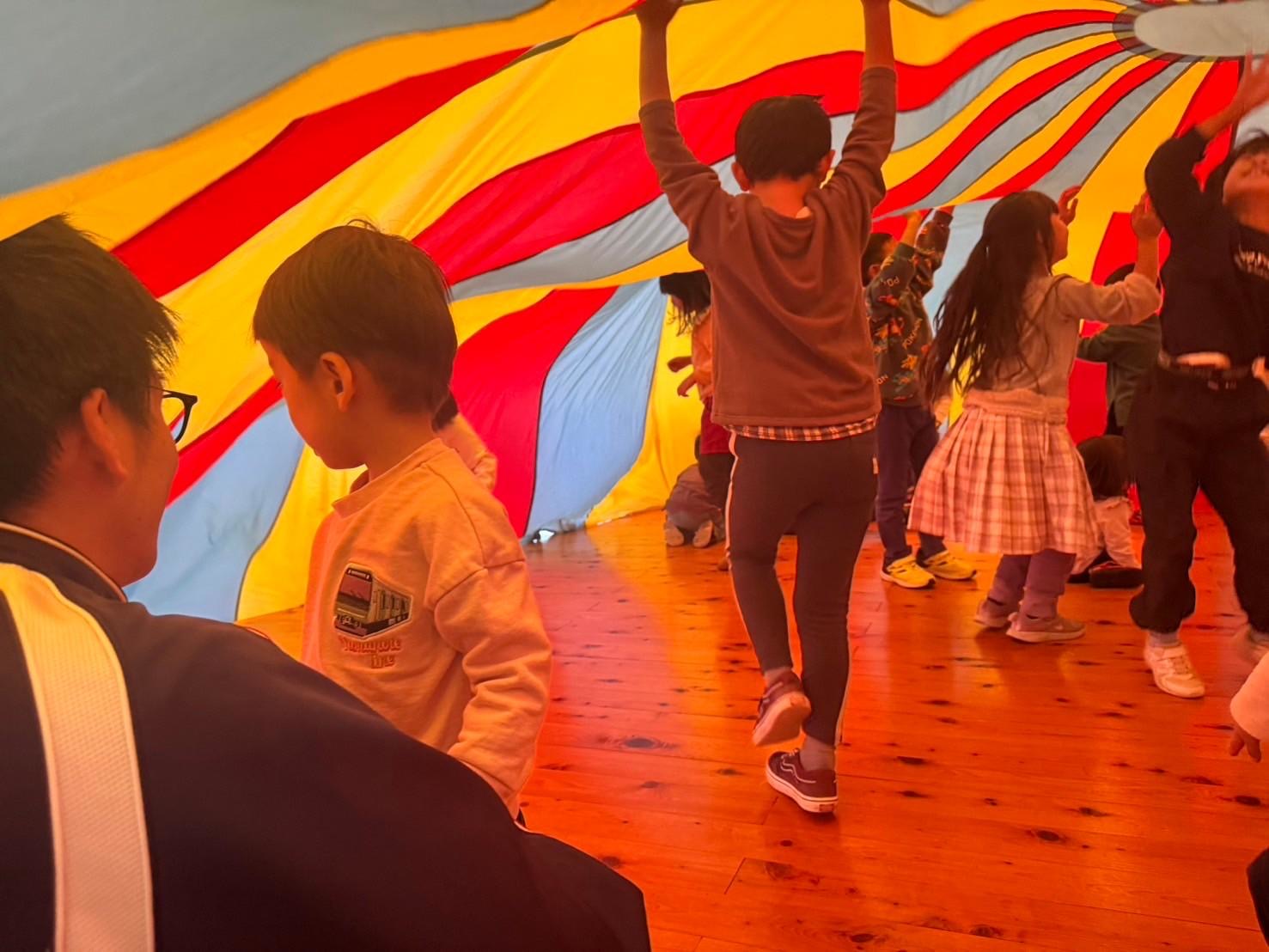 カラフルなパラバルーンの中で踊る子どもたち
