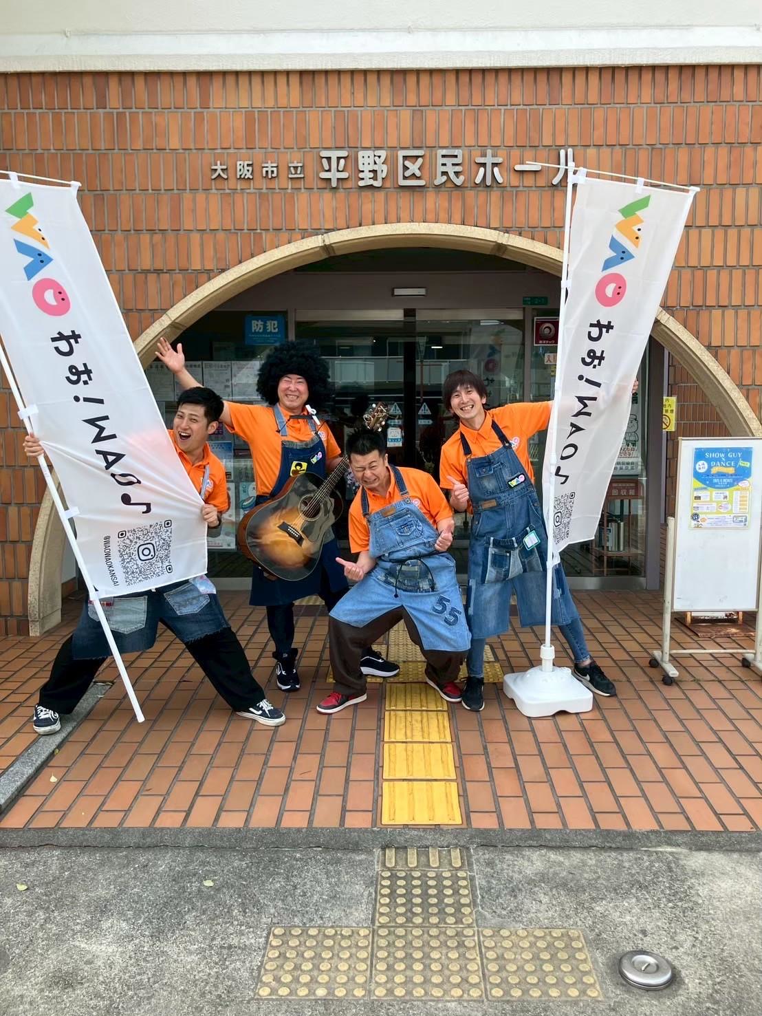 わお！WAO♪ののぼりの前でポーズをとるメンバーたち